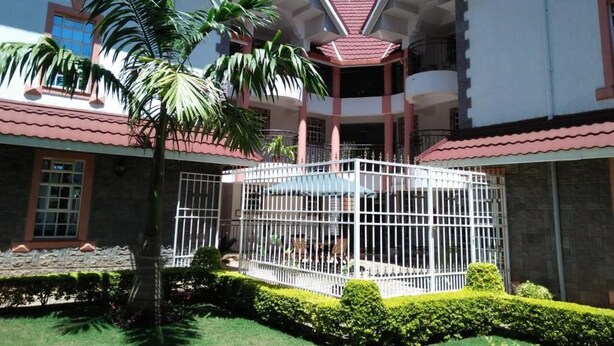 A building with a red-tiled roof, a central courtyard with a white fence, and a palm tree. - Villa Leone (Nairobi)