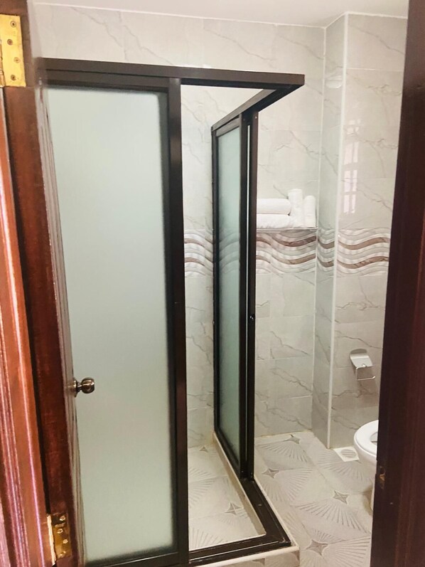 A bathroom with a glass-enclosed shower, marble-patterned walls, a toilet, and a towel rack.