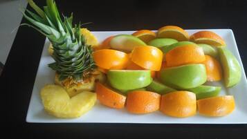 Une assiette rectangulaire blanche garnie de tranches d’ananas, de pommes et d’oranges.