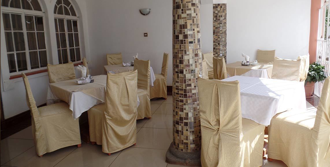 Un espace repas avec des tables et des chaises recouvertes de nappes beiges, une colonne recouverte de carreaux et une fenêtre donnant sur un paysage agréable.
