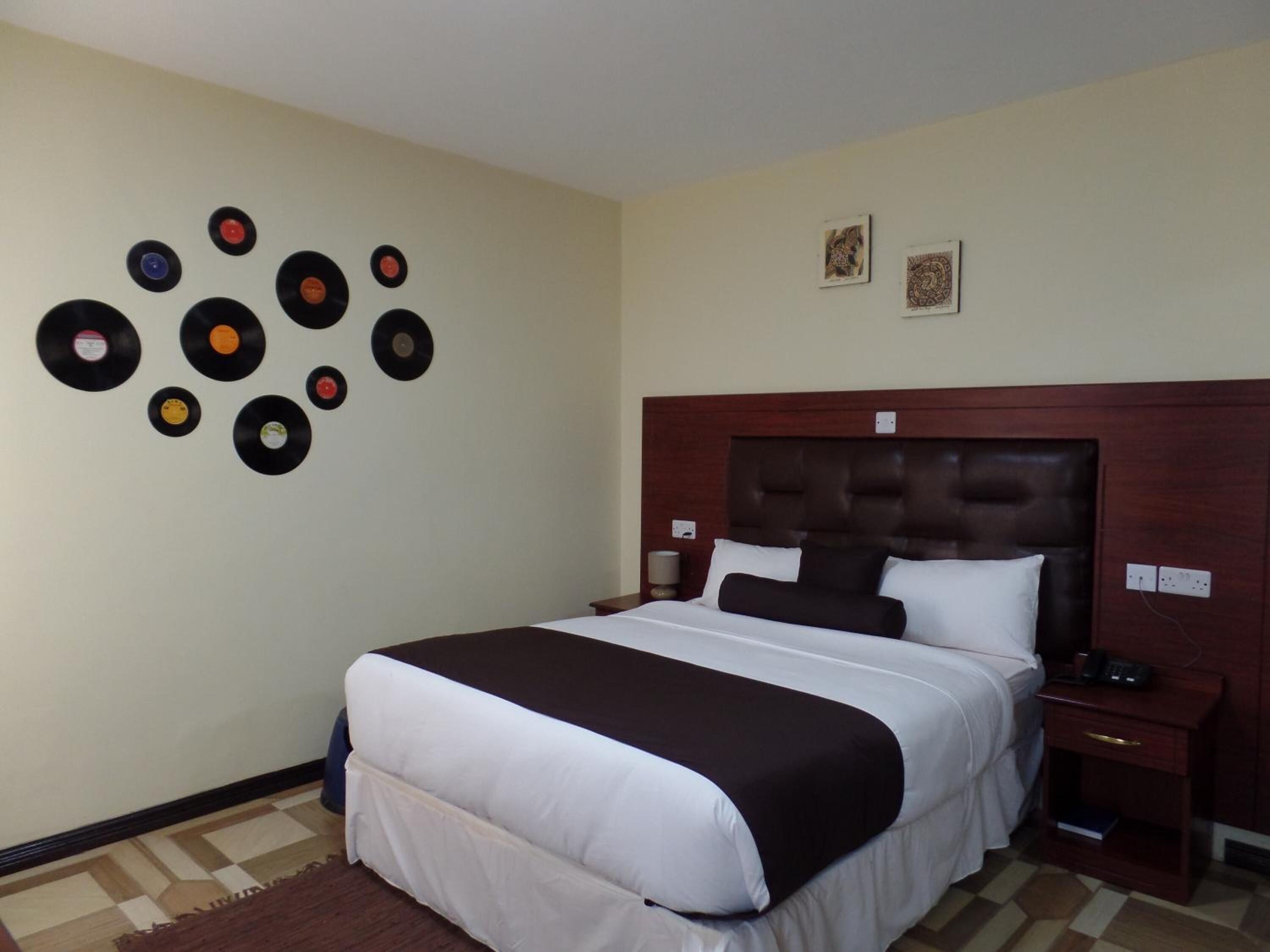 A hotel room with a large bed, a wooden headboard, a nightstand, and a wall decorated with vinyl records.