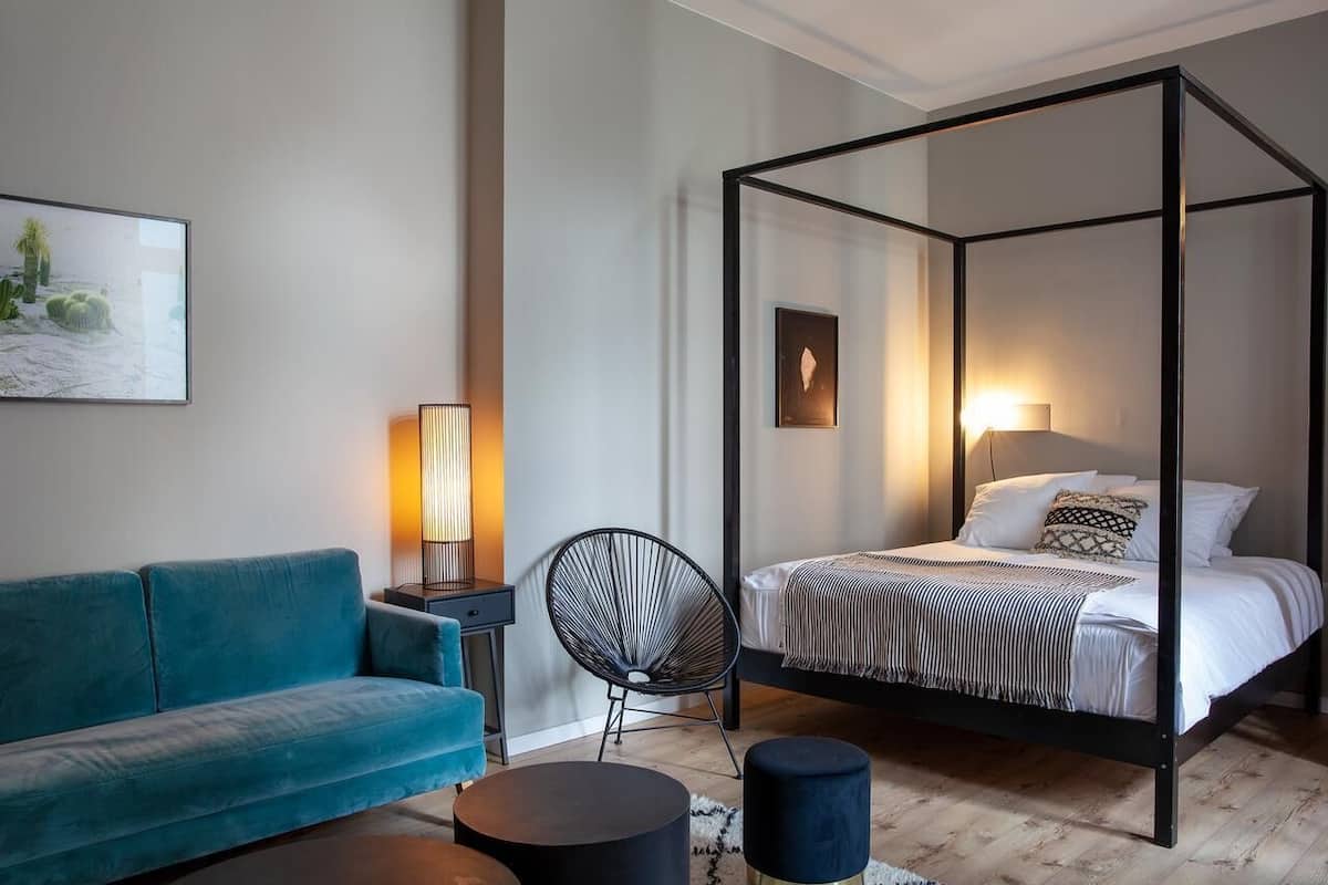 A modern bedroom with a four-poster bed, a blue sofa, a round coffee table, and a chair.
