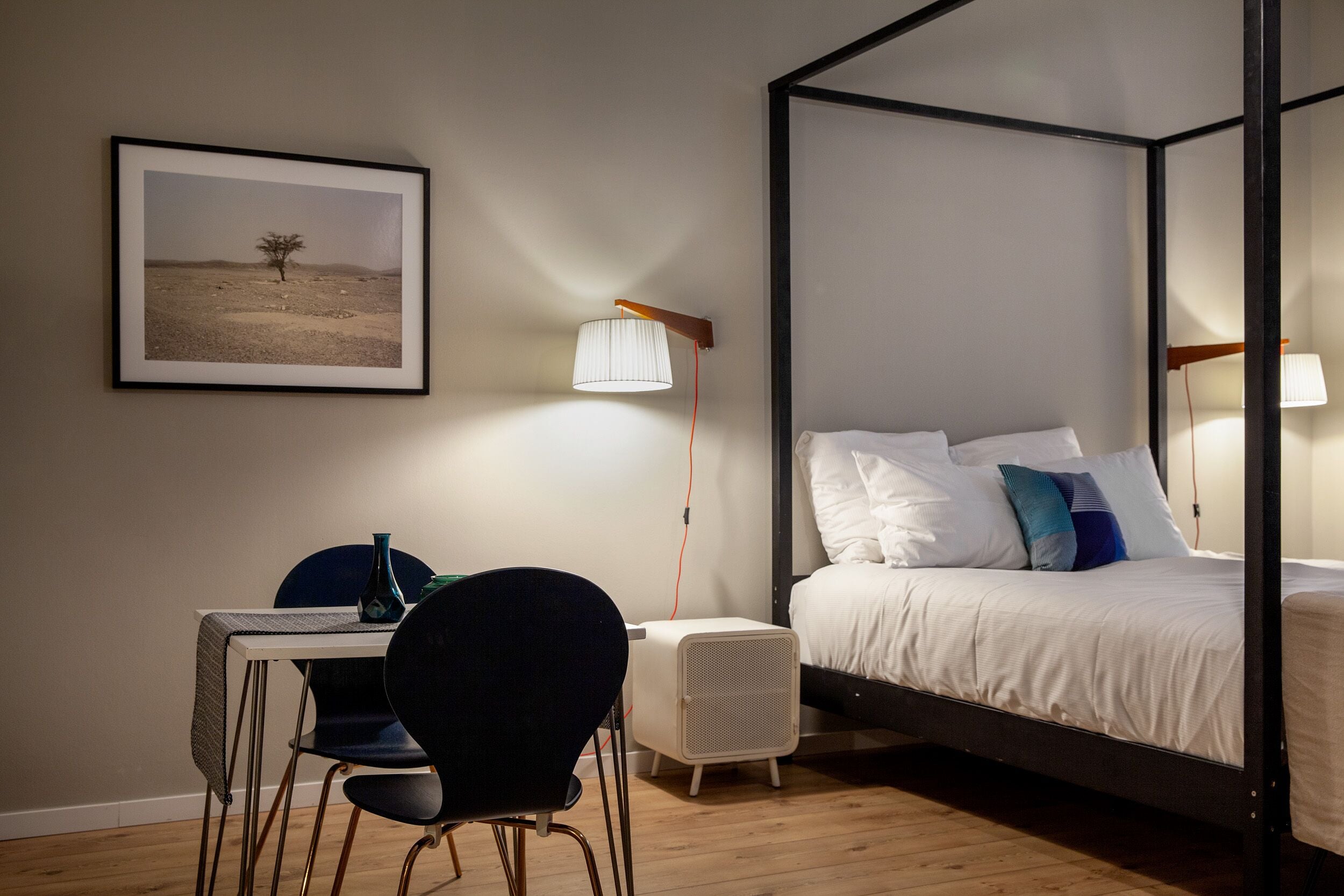 Quarto com cama de dossel, escrivaninha com cadeira, mesa de cabeceira e quadro na parede.