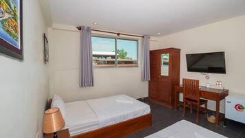 Quarto de hotel com cama, escrivaninha, televisão e janela com cortinas.