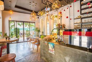 A modern cafe with a concrete counter, hanging lights, and a view of greenery outside. - Le Water Villa (Siem Reap)