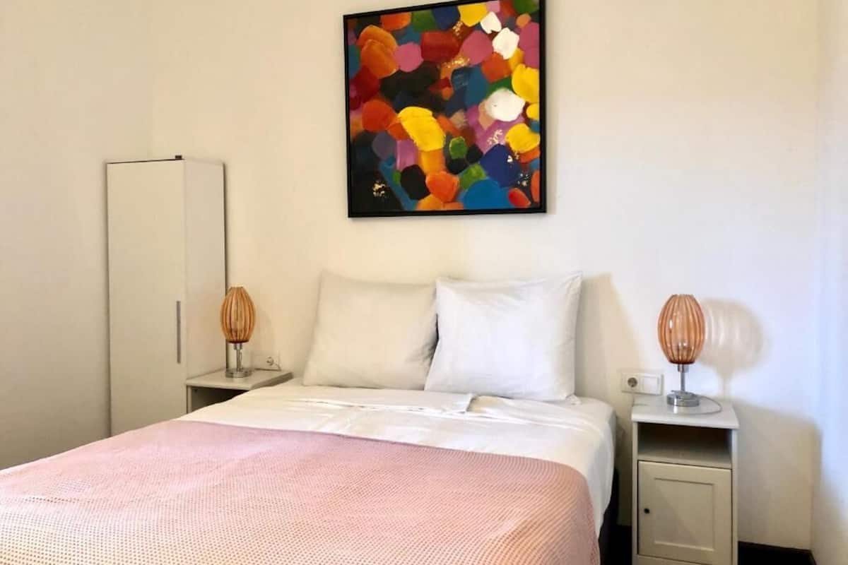 A bedroom with a bed, a wardrobe, bedside tables, and a colorful abstract painting on the wall.