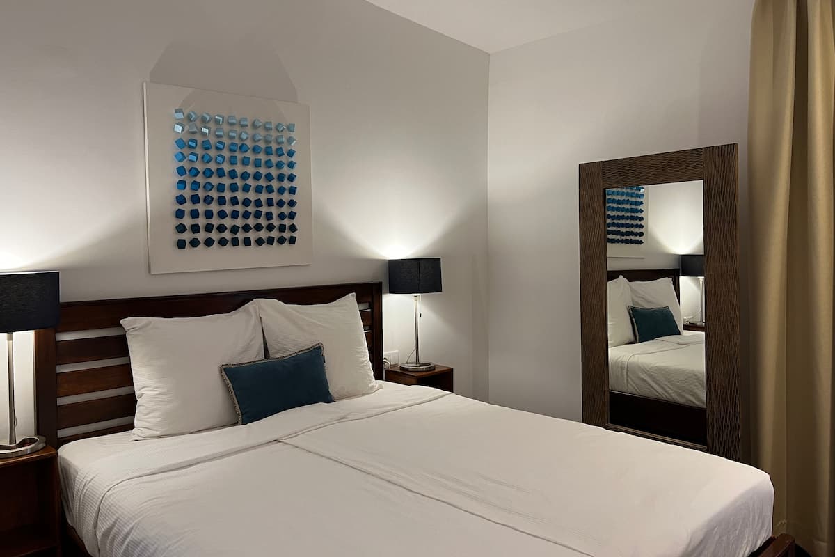 A hotel room with a large bed, two bedside tables with lamps, a wall-mounted artwork, and a mirror.