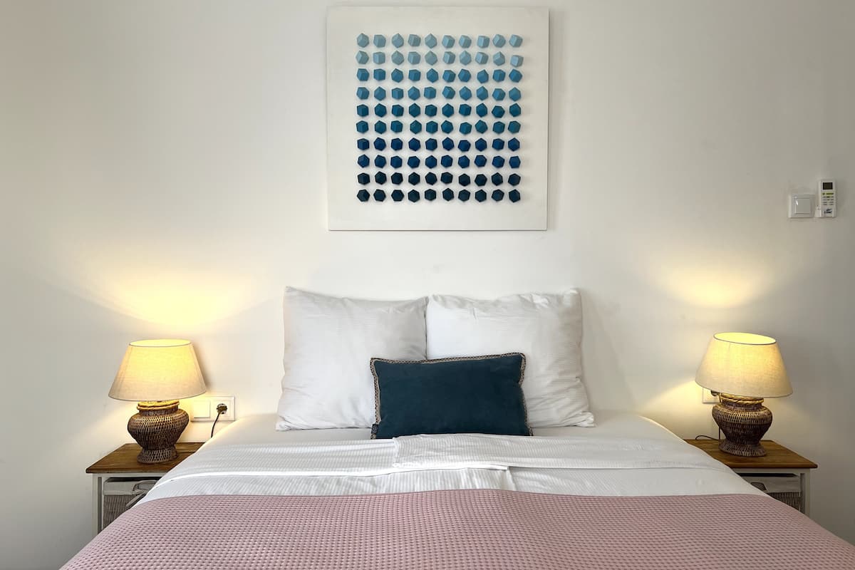 A neatly arranged hotel room with a bed, two bedside lamps, a wall-mounted artwork, and a thermostat.