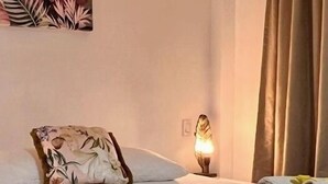A hotel room with a bed, a nightstand, a lamp, and a tropical-themed painting on the wall. - Villa Famiri (Paramaribo)