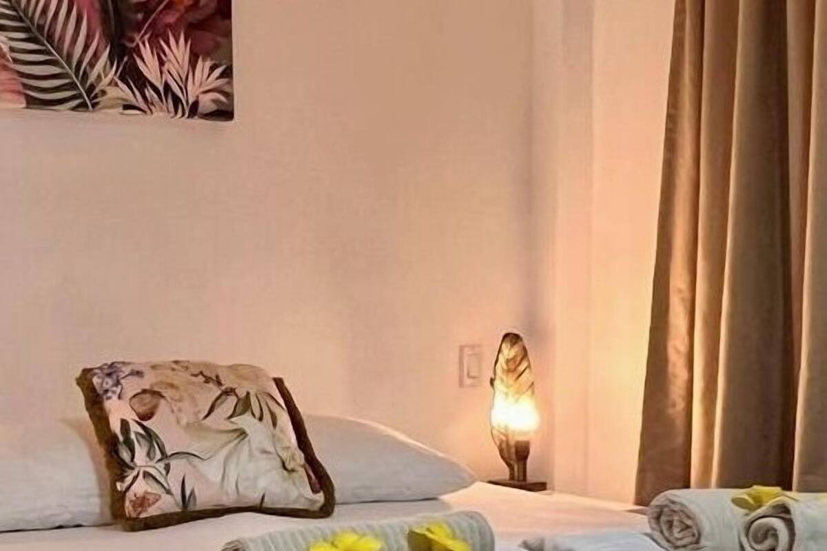 A hotel room with a bed, a nightstand, a lamp, and a tropical-themed painting on the wall.