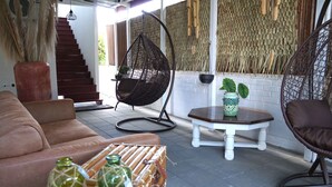 A cozy living area with a brown sofa, wicker chairs, a small table, and a staircase. - Villa Famiri (Paramaribo)