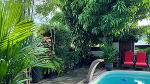 A swimming pool with a tiled deck, surrounded by lush greenery and red chairs. - Villa Famiri (Paramaribo)