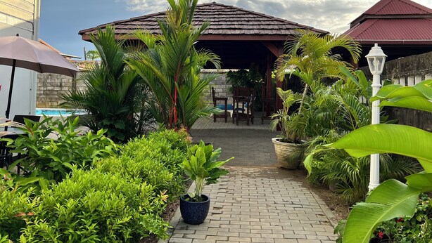 A pathway leading to a covered area with a tiled roof, surrounded by lush greenery and potted plants. - Villa Famiri (Paramaribo)