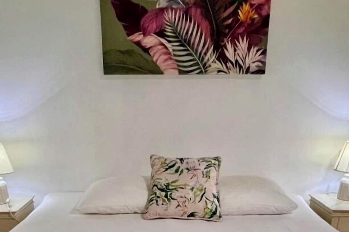 A neatly made bed with a floral pillow, two towels, and a wall-mounted painting.