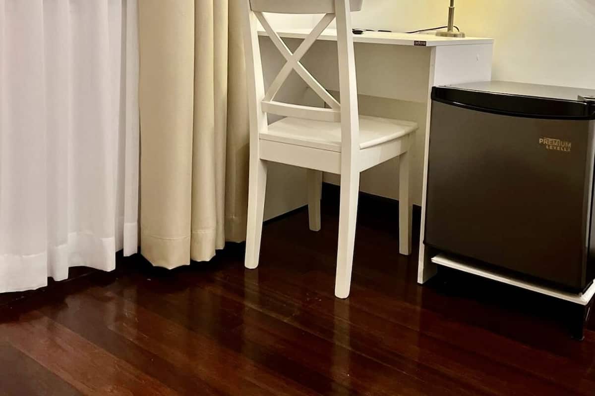A room with a white chair, a desk, a television mounted on the wall, a red lamp, and a compact refrigerator.