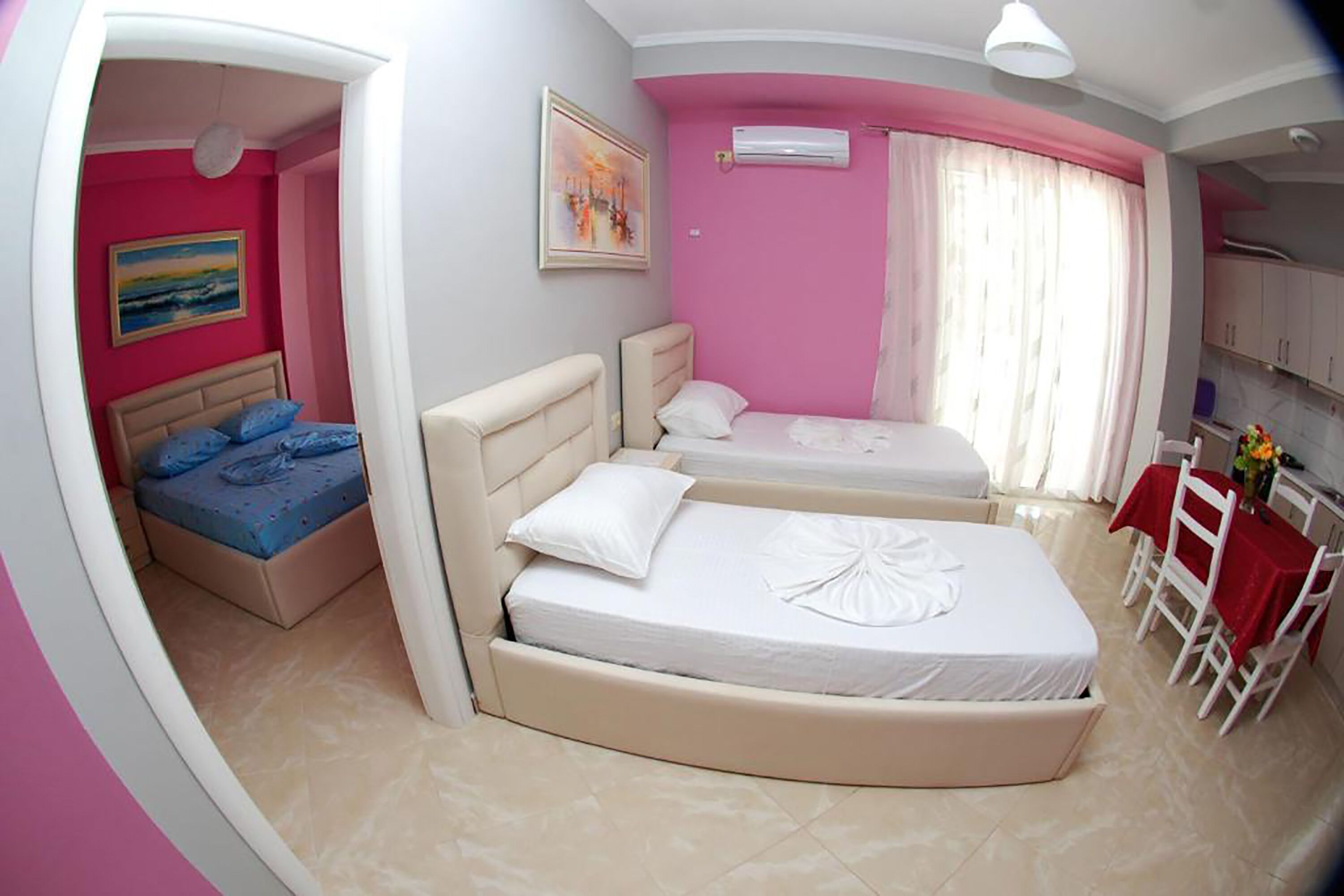 A bedroom with two beds, a dining area with a table and chairs, and a painting on the wall.