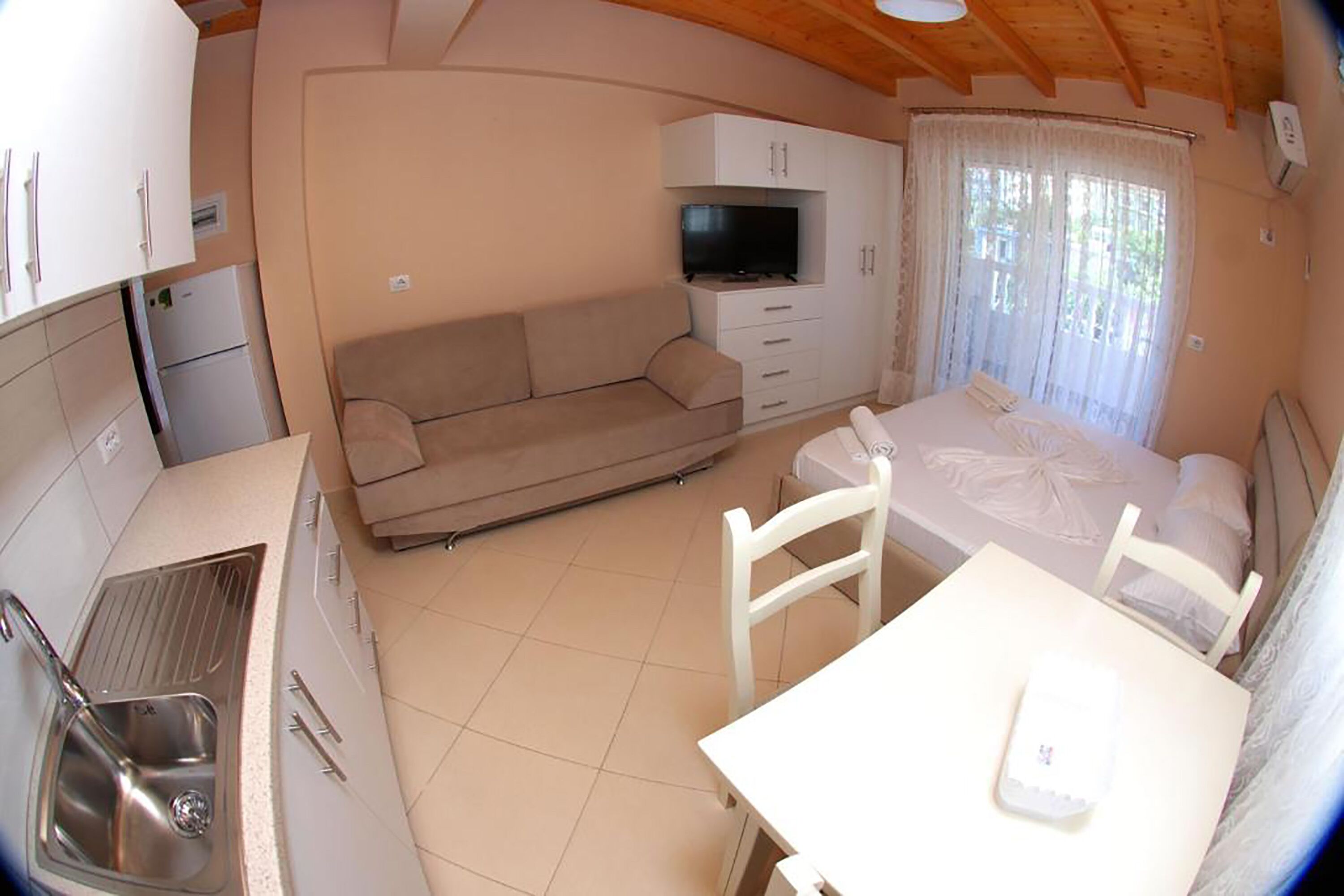 Un espacio habitable pequeño con kitchenette, sofá, cama y televisor.
