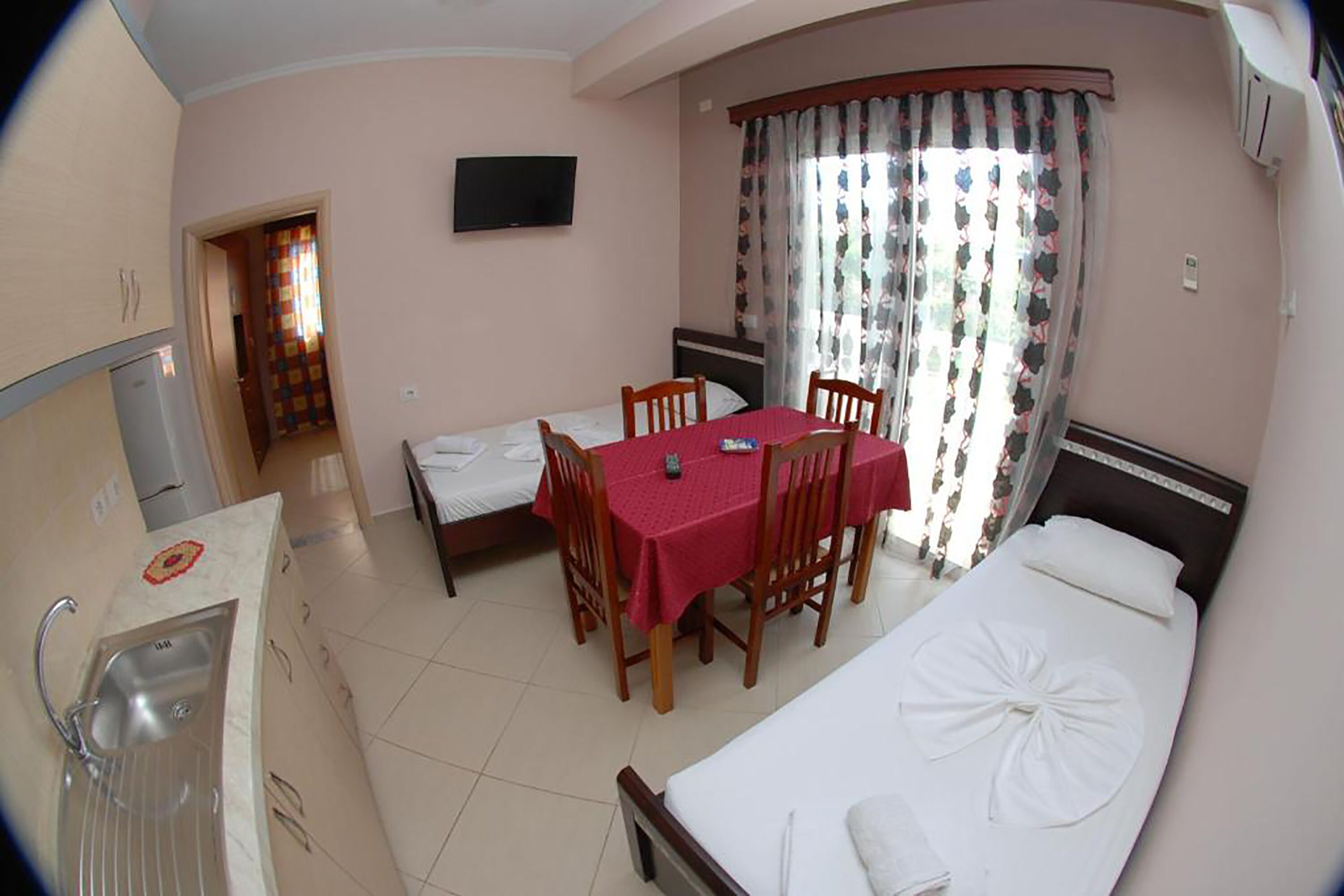 Quarto de hotel pequeno e funcional, com uma cama de solteiro, uma mesa com cadeiras, uma kitchenette e um banheiro.