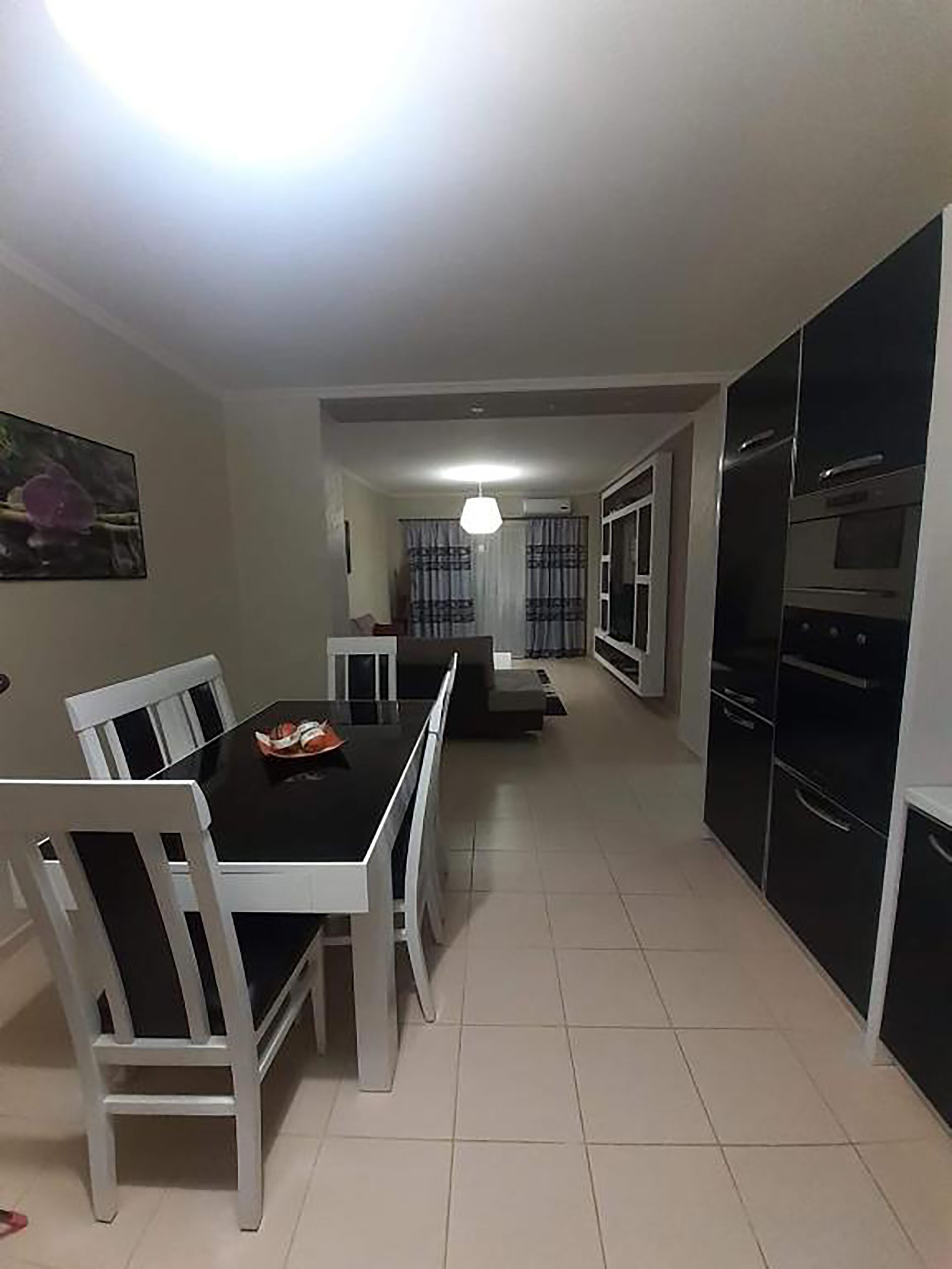 A modern kitchen with black appliances, a dining area with white chairs, and a visible ceiling light.