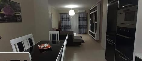 A modern kitchen with black appliances, a dining area with white chairs, and a visible ceiling light.