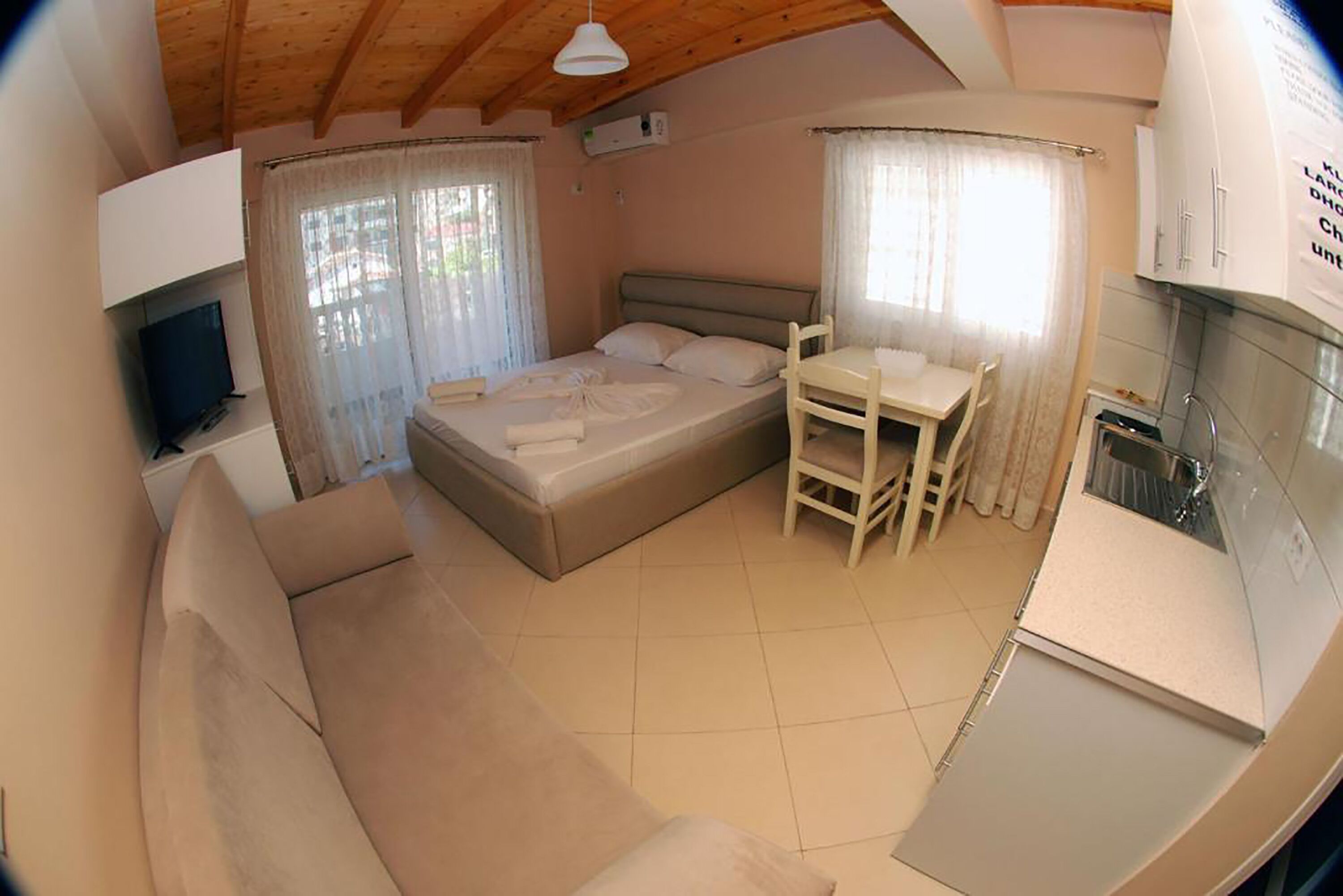A compact bedroom with a bed, a small table, a sofa, and a kitchenette.
