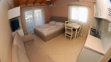 A compact bedroom with a bed, a small table, a sofa, and a kitchenette.