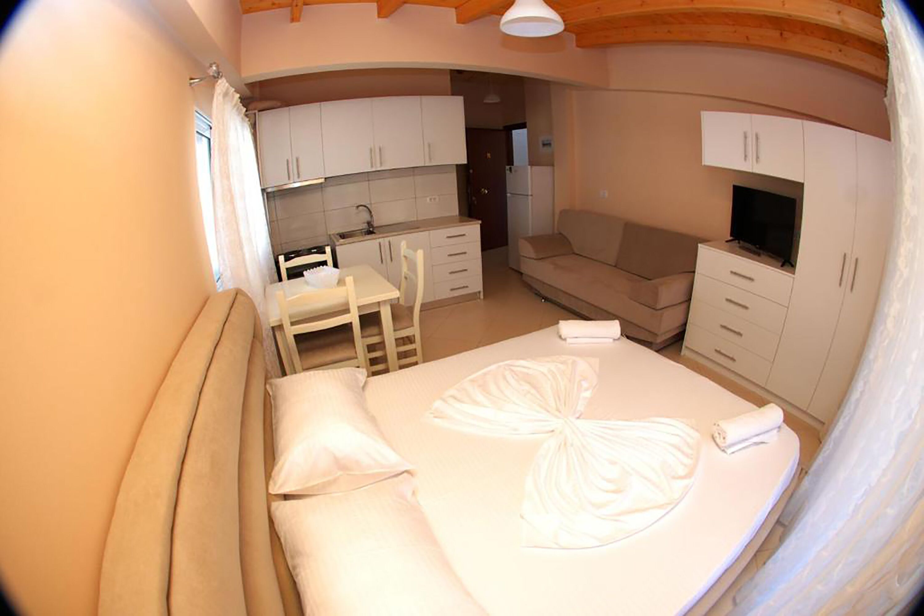 Een compacte slaapkamer met een bed, een klein tafeltje en een bank. In de achtergrond bevindt zich een kitchenette.