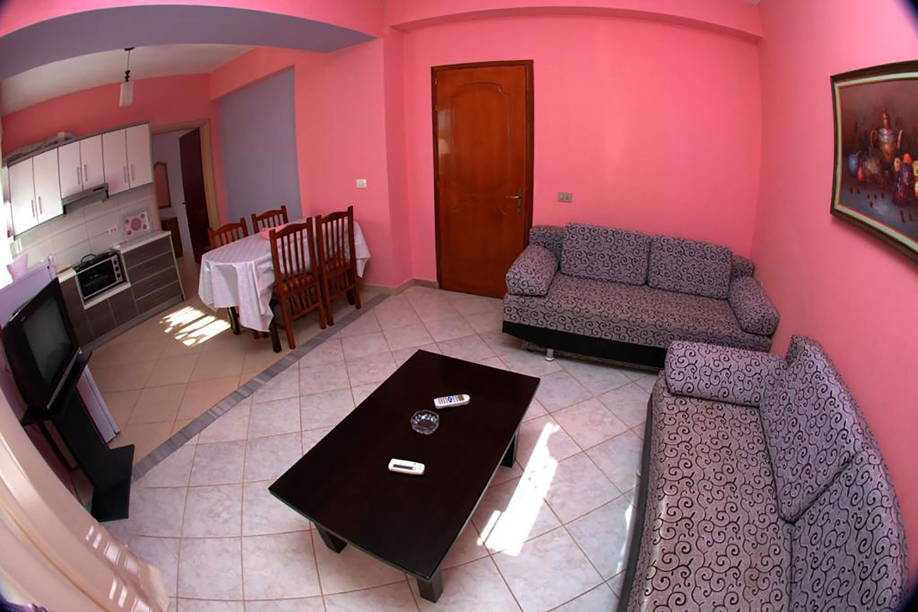 Un salon comprenant un canapé, une table basse, un téléviseur, un coin cuisine et une porte.