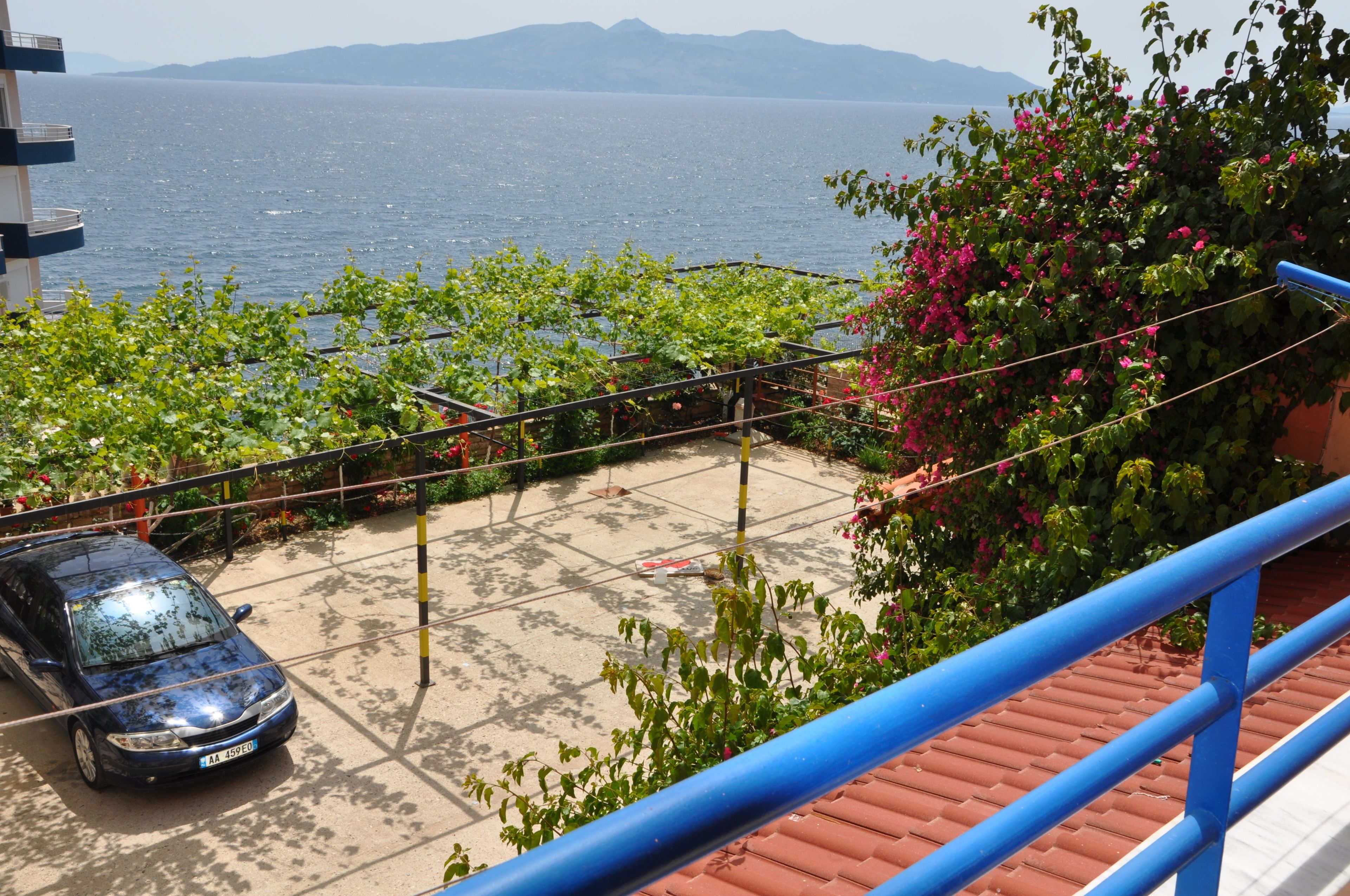 Un balcon avec vue sur la mer, une voiture garée et une rambarde.
