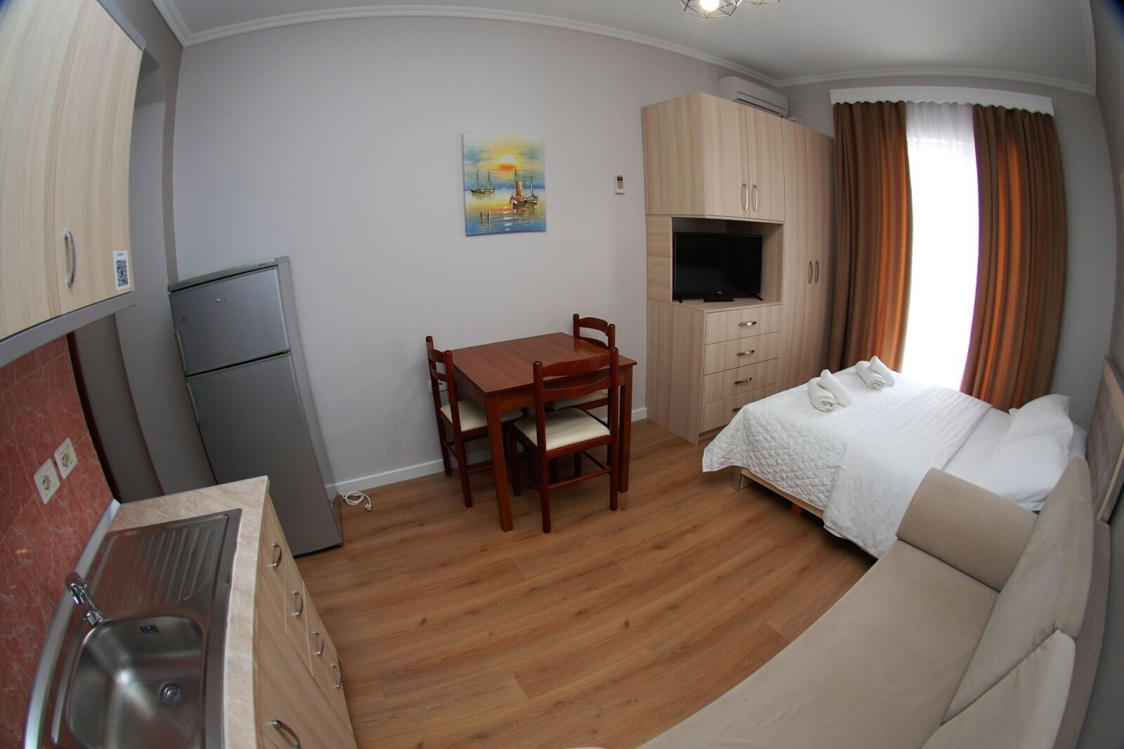 Een compacte kamer met een kitchenette, een eettafel, een bed en een televisie.