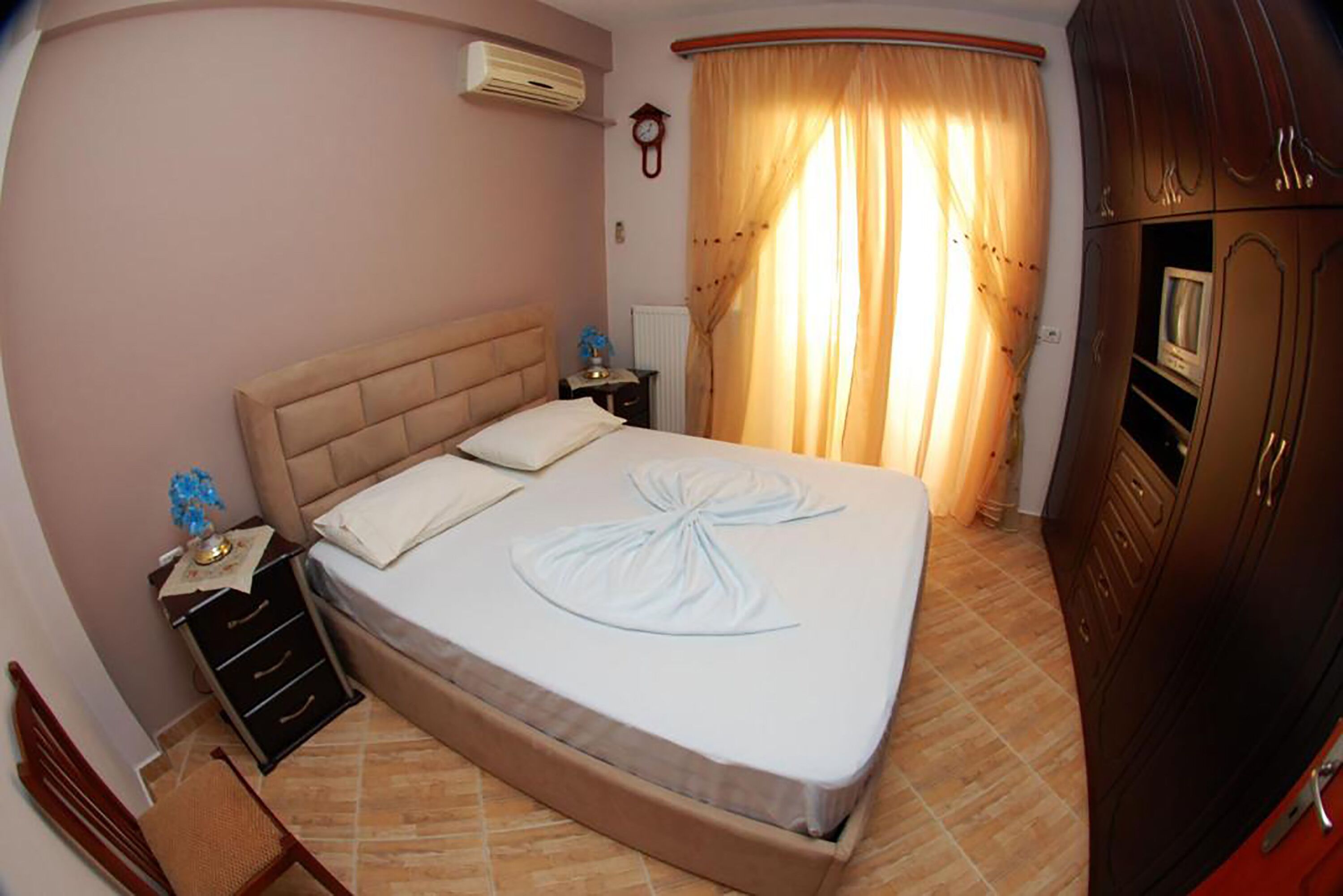 Un dormitorio con cama, mesitas de noche, un reloj, cortinas y un armario.