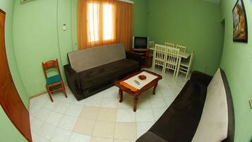 Una sala de estar con sofá, una mesita, televisor y un comedor con sillas.