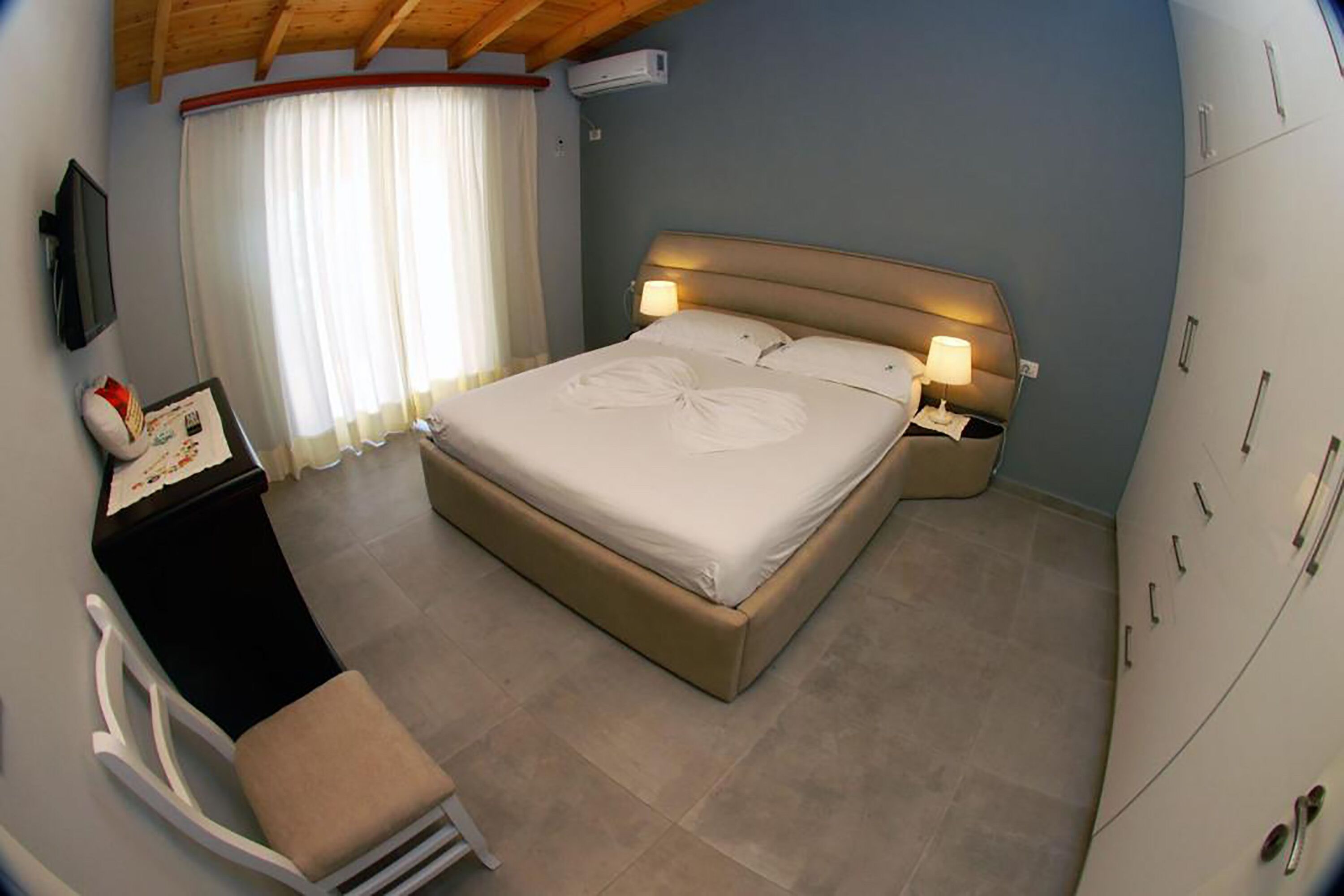Ein Schlafzimmer mit einem Bett, Nachttischlampen, einem Schreibtisch und einem Sessel.