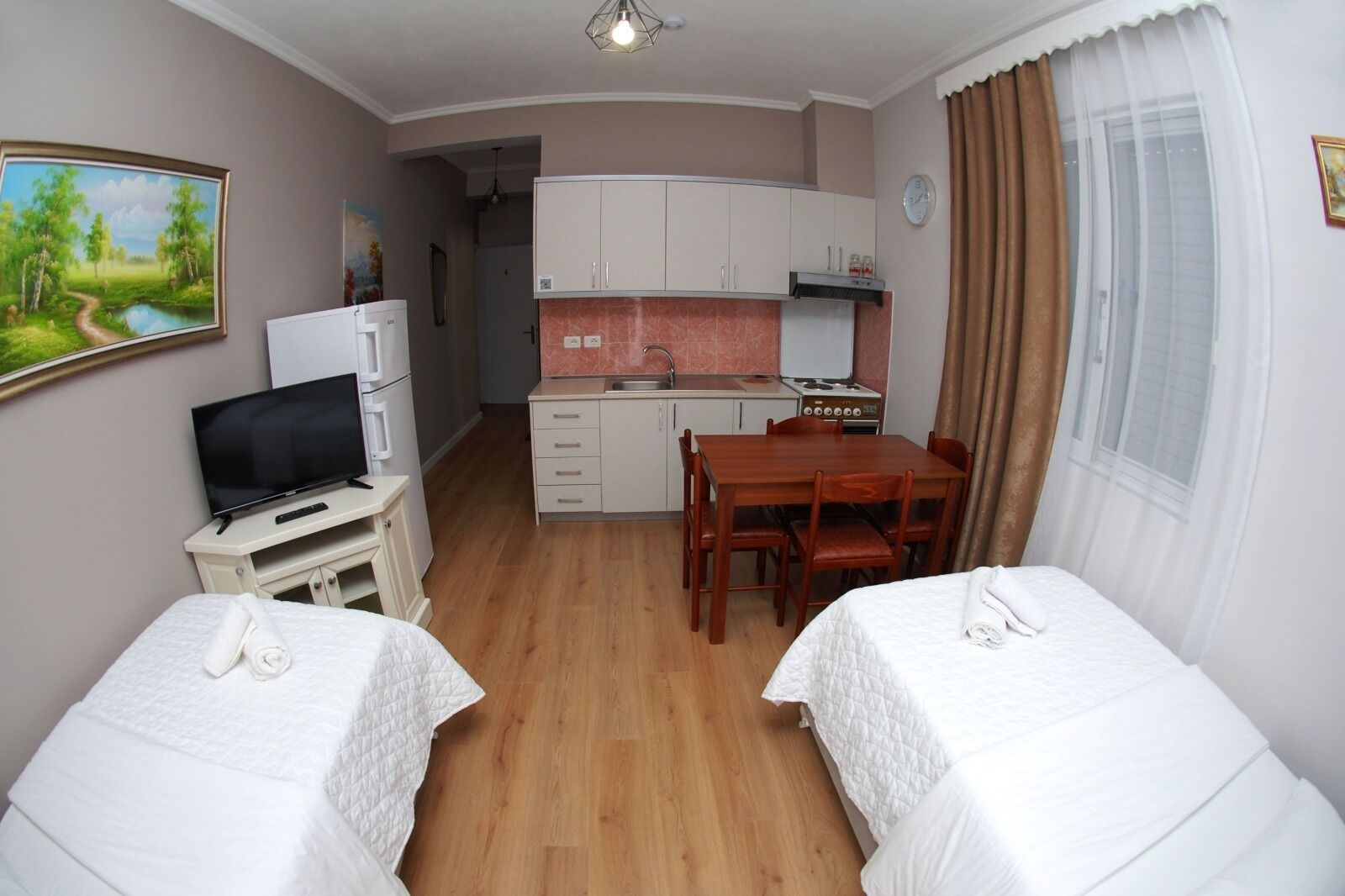 A hotel room with two beds, a TV, a small kitchenette, and a dining table.
