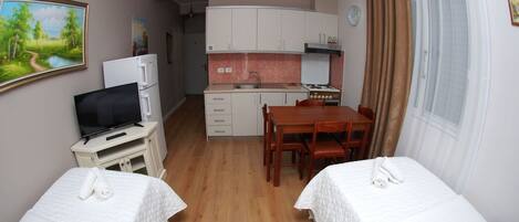 A hotel room with two beds, a TV, a small kitchenette, and a dining table.