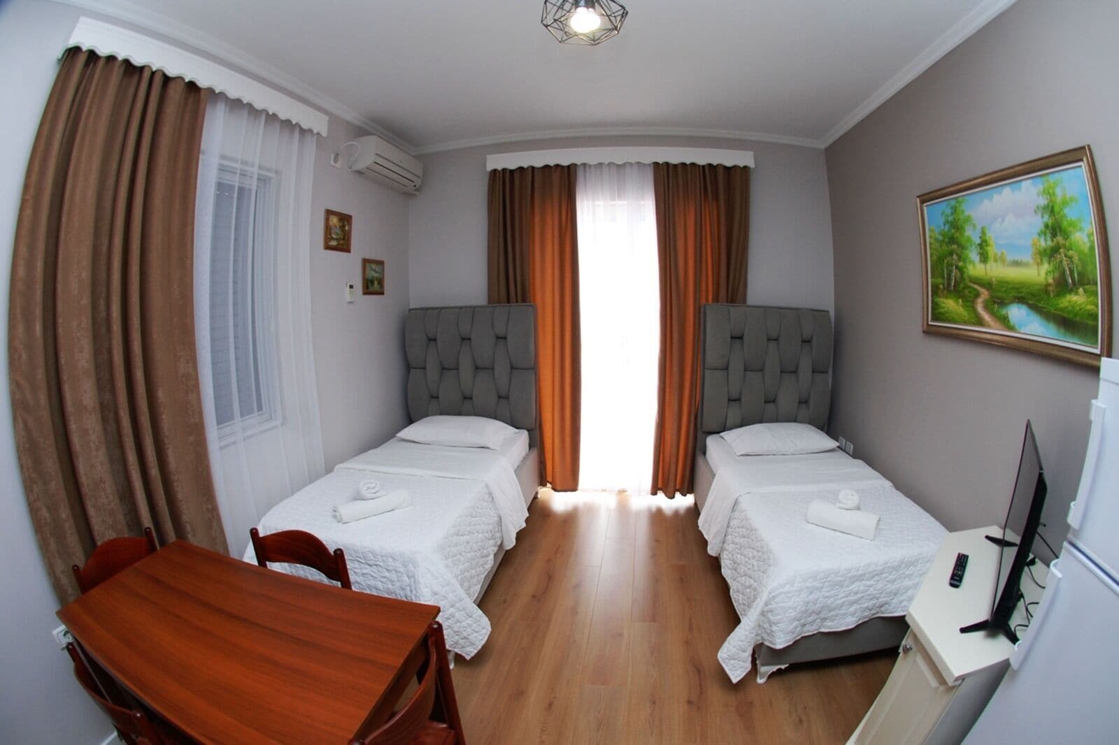 A room with two single beds, a wooden table, a TV, and a painting on the wall.