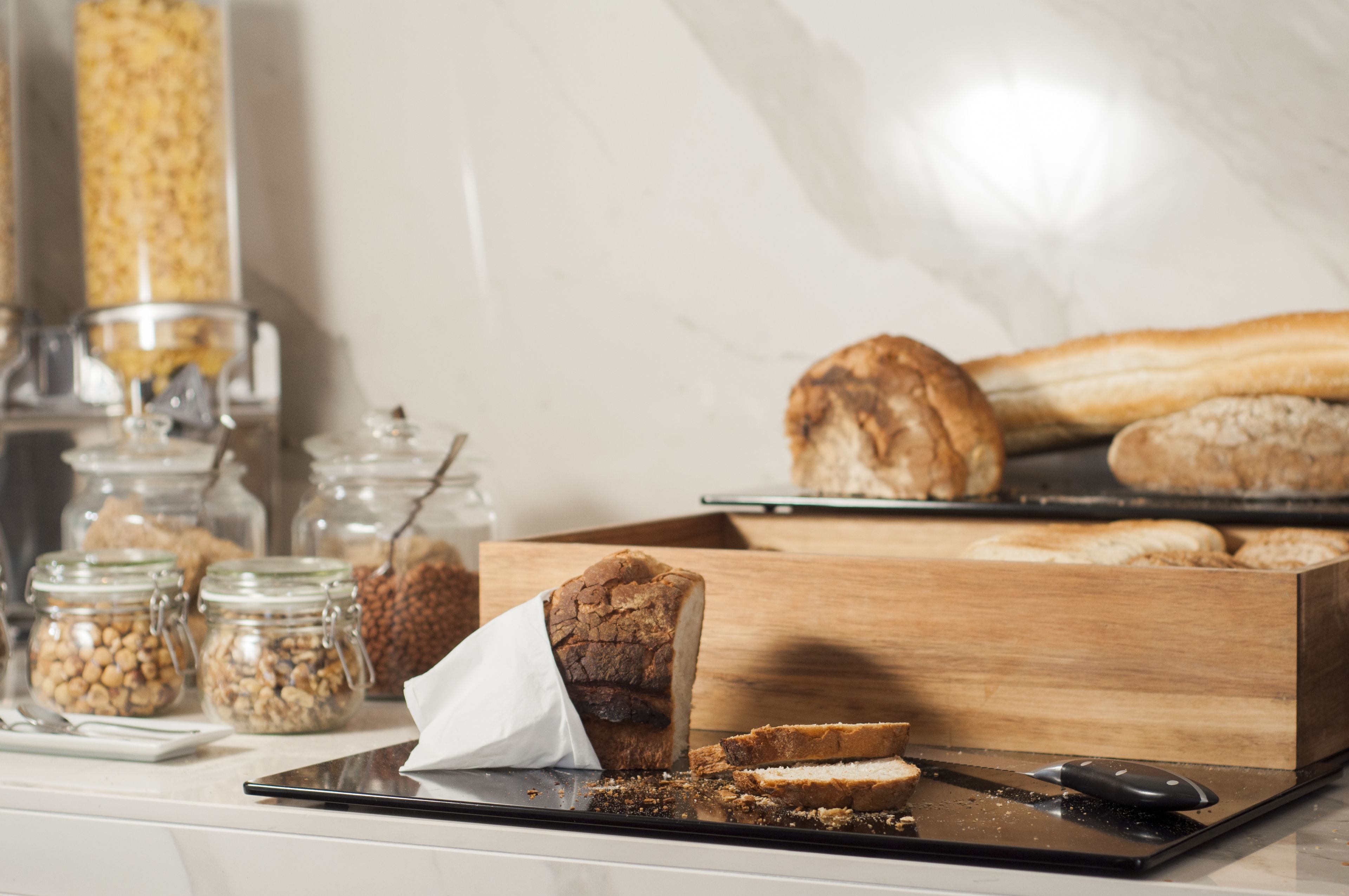 Un plan de travail de cuisine avec des bocaux de noix, une miche de pain et une planche à découper sur laquelle sont disposées des tranches de pain.