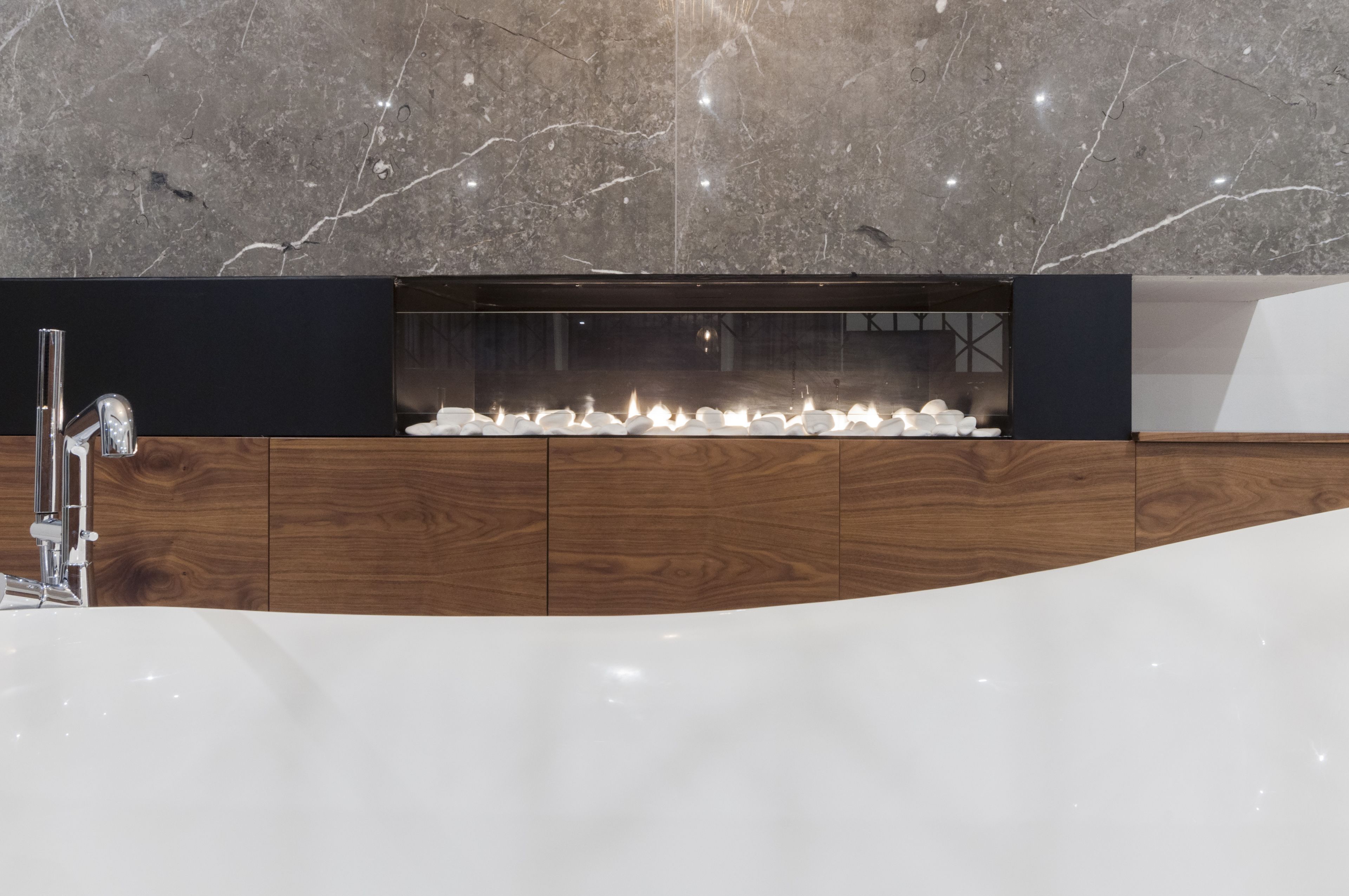 Une salle de bain moderne avec un pare-baignoire en marbre, un meuble-lavabo en bois et un élément décoratif intégré avec de l’eau.