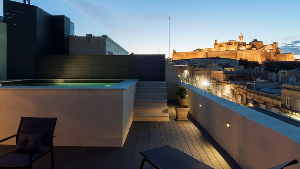 A rooftop terrace with a hot tub, lounge chairs, and a view of a historic city wall at dusk. - The Duke Boutique Hotel (Victoria)