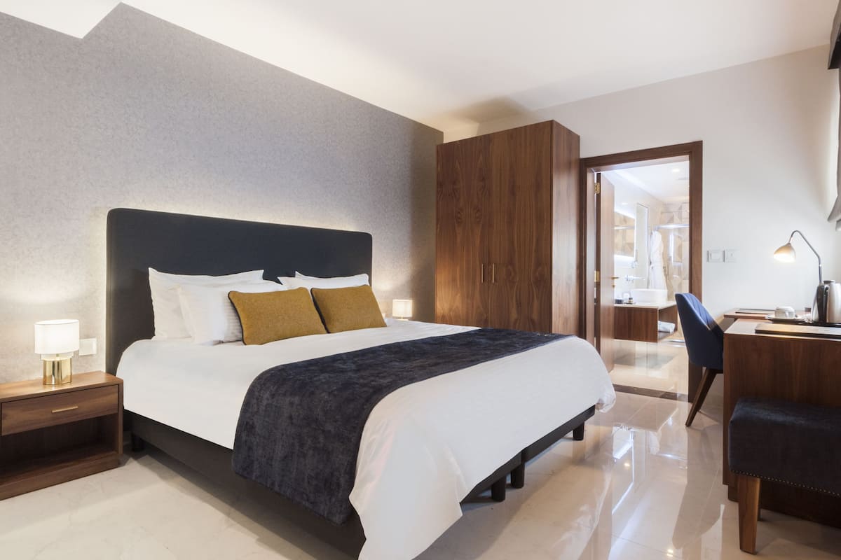 A modern bedroom with a large bed, wooden wardrobe, and a desk with a chair.