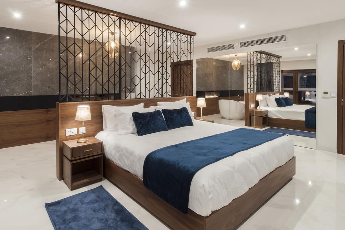 A modern bedroom with a large bed, wooden headboard, bedside tables, and a mirror.