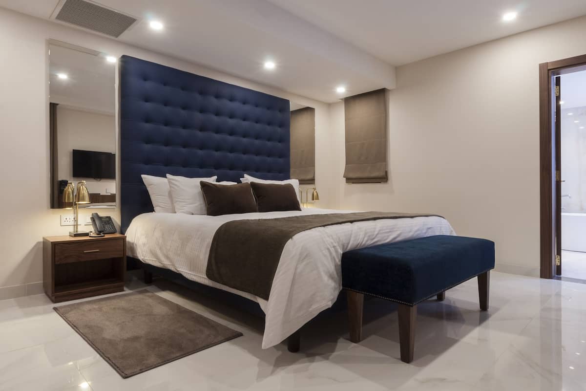 A modern bedroom with a large bed, a bedside table with a lamp, and a mirror.
