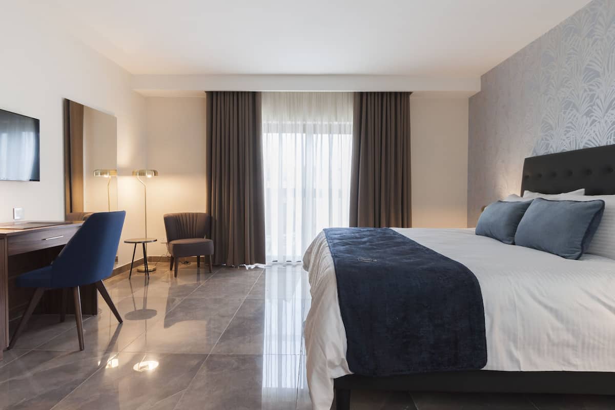 A hotel room with a large bed, a desk, a chair, and a television.