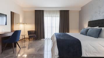 A hotel room with a large bed, a desk, a chair, and a television.