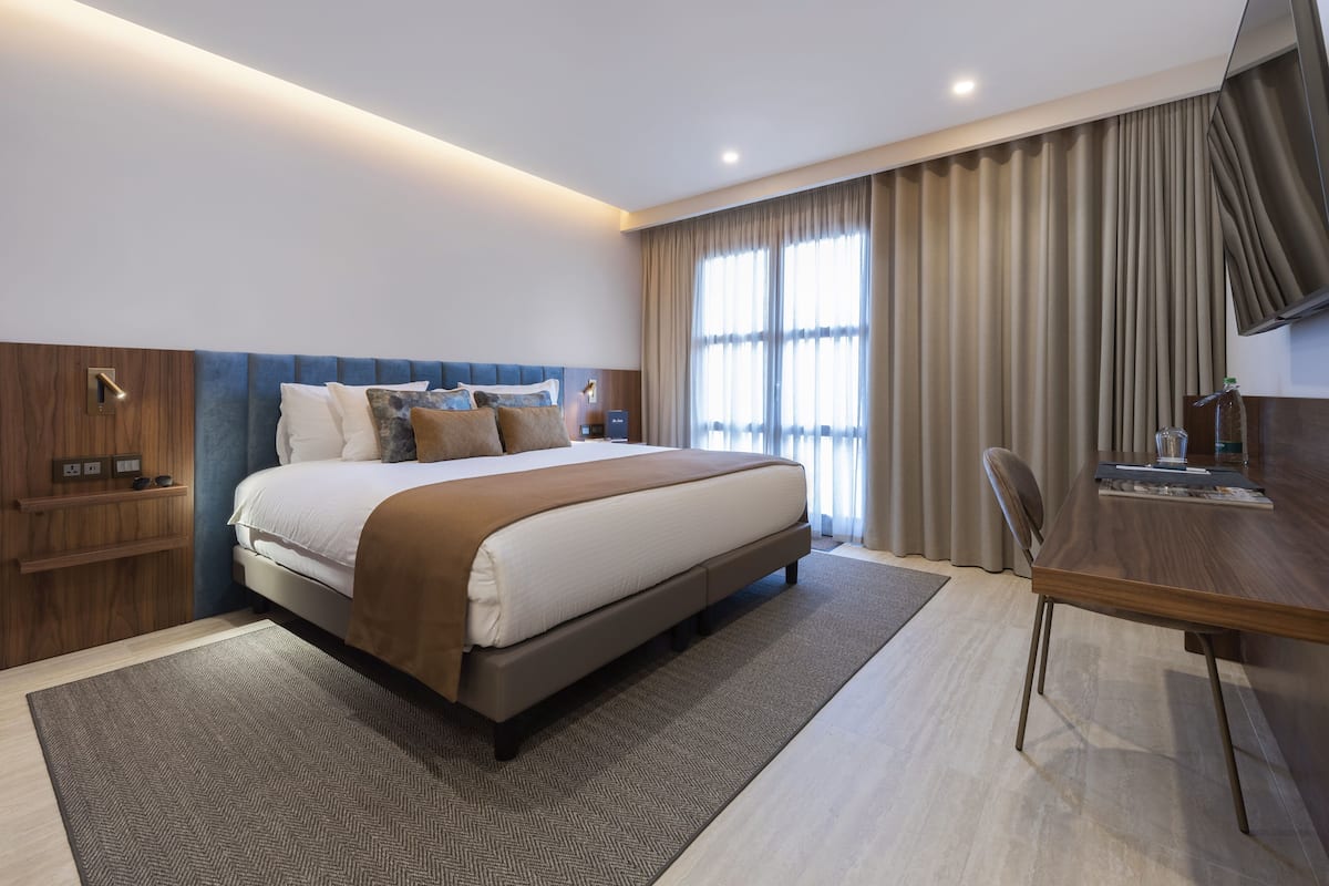 A modern hotel room with a large bed, a desk, and a television.