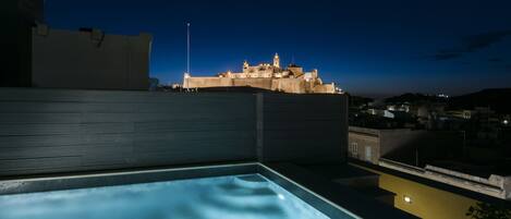 A rooftop pool with a view of a historic building at dusk.