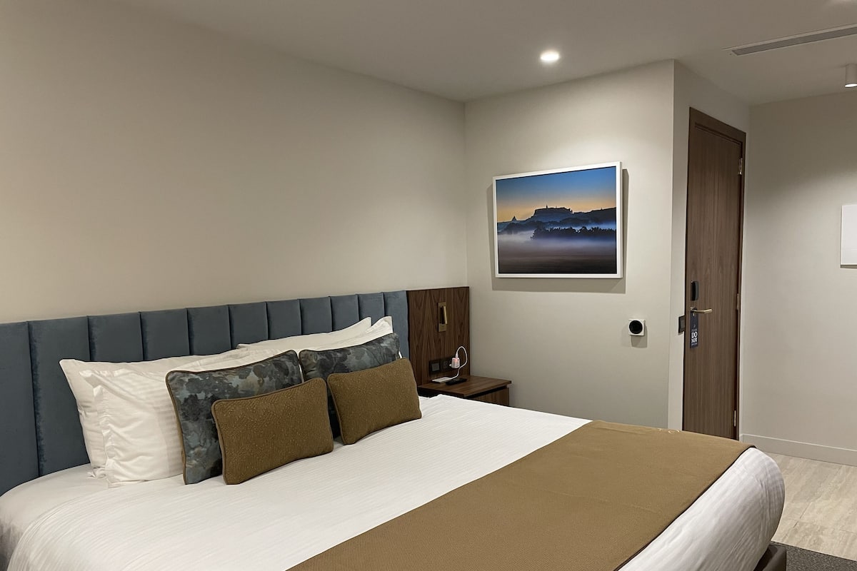 A hotel room with a bed, a nightstand, a wall-mounted picture, and a door.