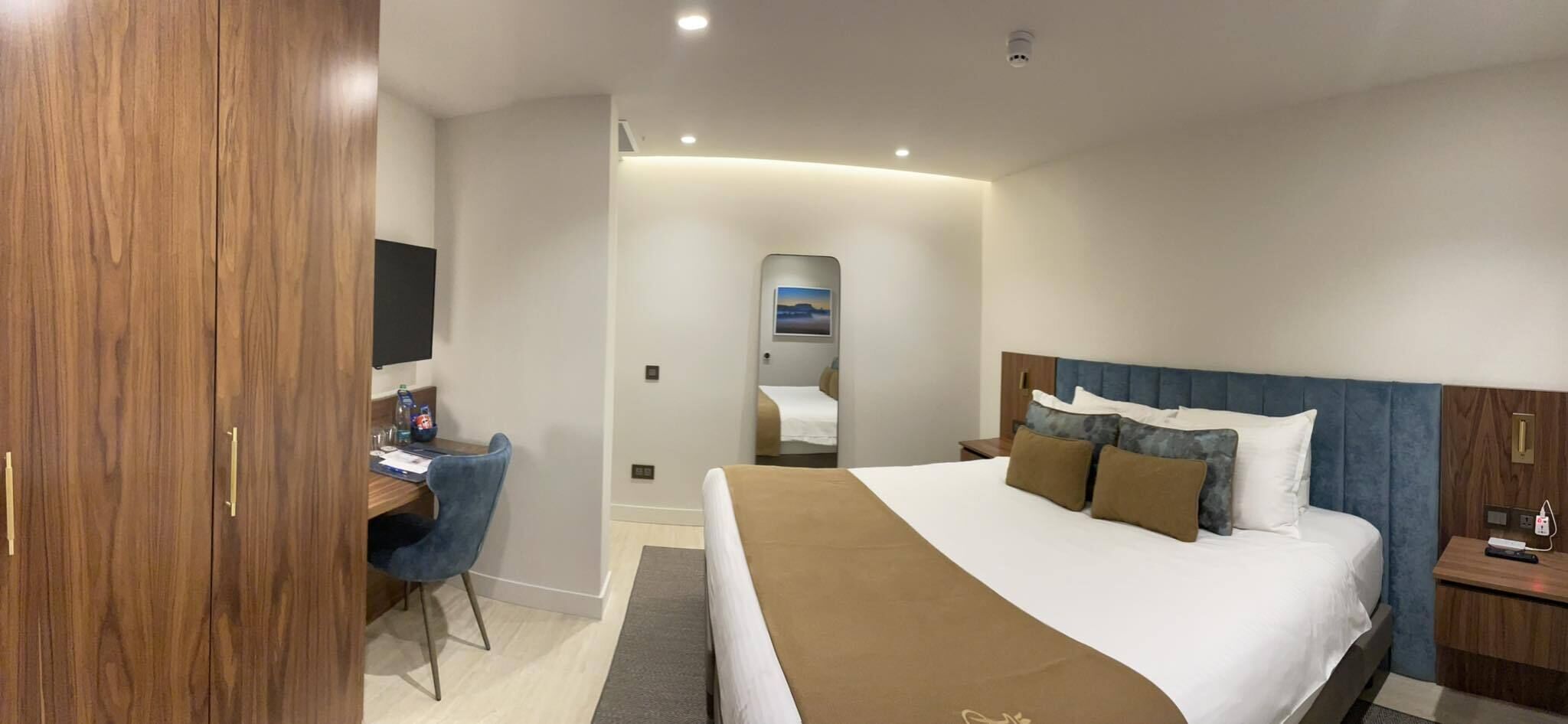 A hotel room with a bed, a desk, a chair, a TV, and a mirror.