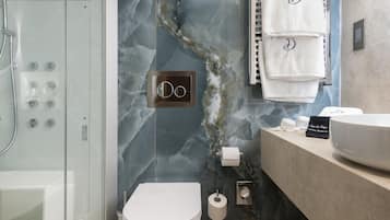 Un baño moderno con ducha de vidrio, pared de mármol, inodoro blanco y tocador con lavamanos grande y espejo.