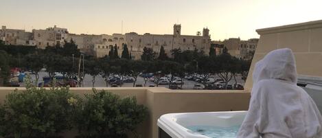 A person sitting by a hot tub overlooking a parking lot and buildings.